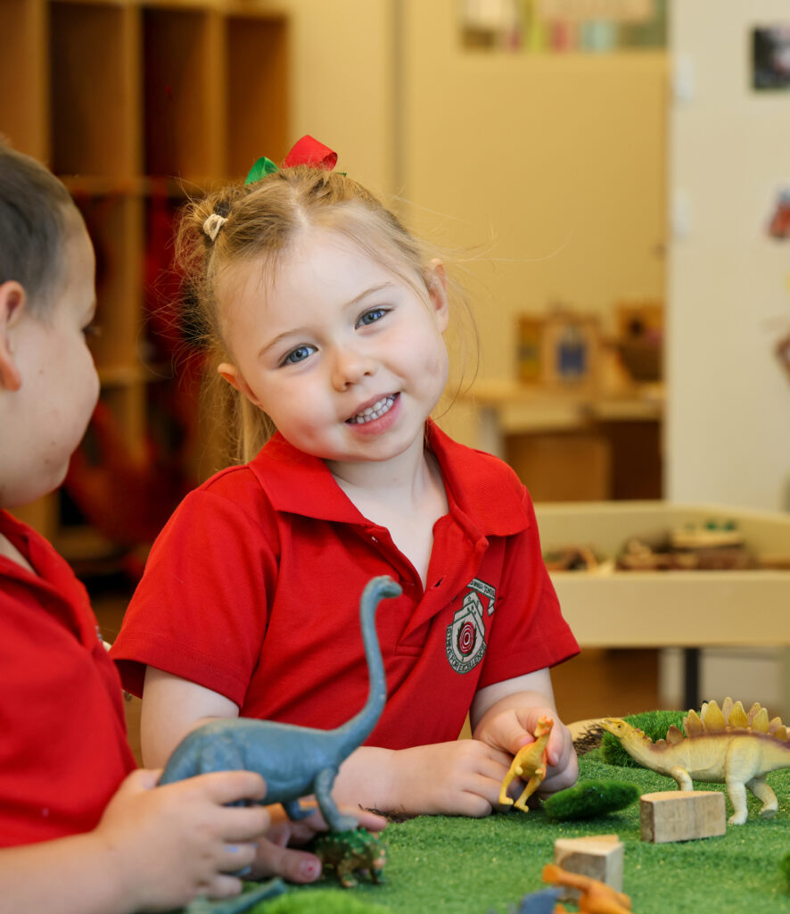 Young boy wearing a red tee shirt sitting at a desk smiling to camera